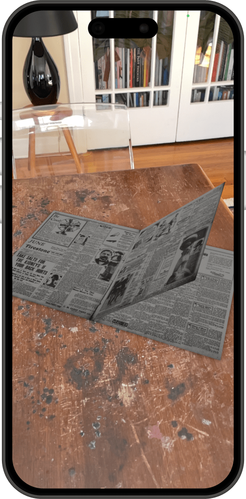 Screenshot of the Booksnake app on an iPhone 14, showing a digitized newspaper on a physical table, with one page of the newspaper in the process of turning